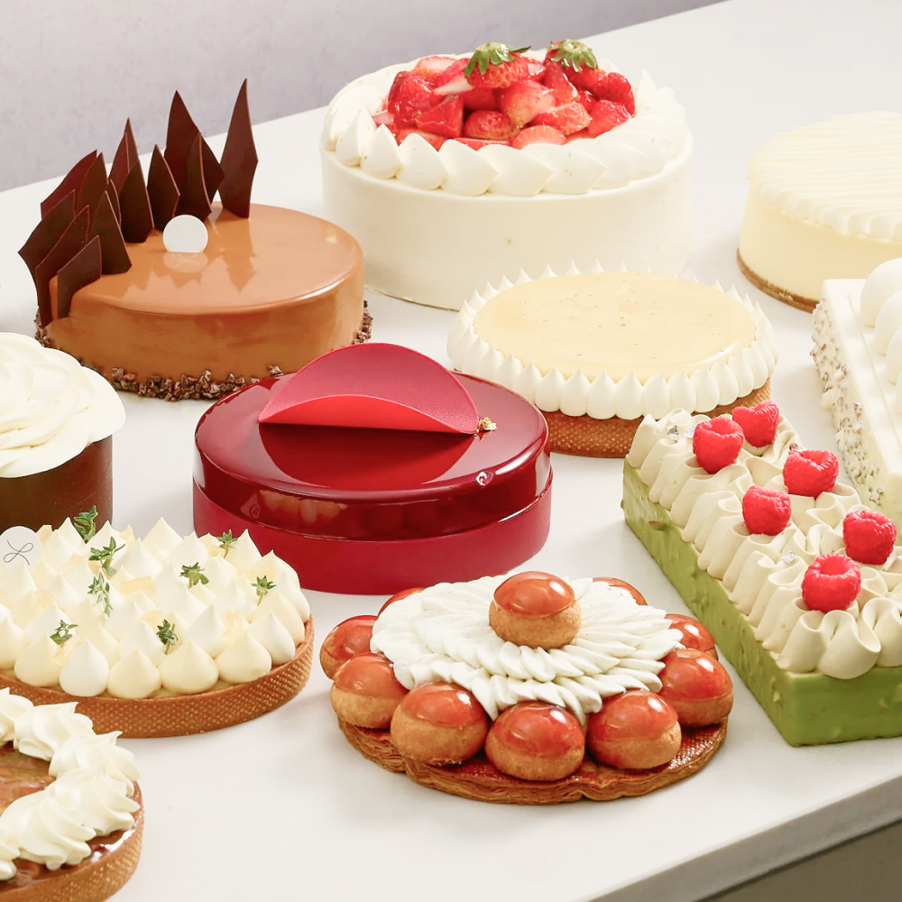 an assortment of cakes and tarts with some fruit decorations, some are red, green, and pale yellow and some are shiny