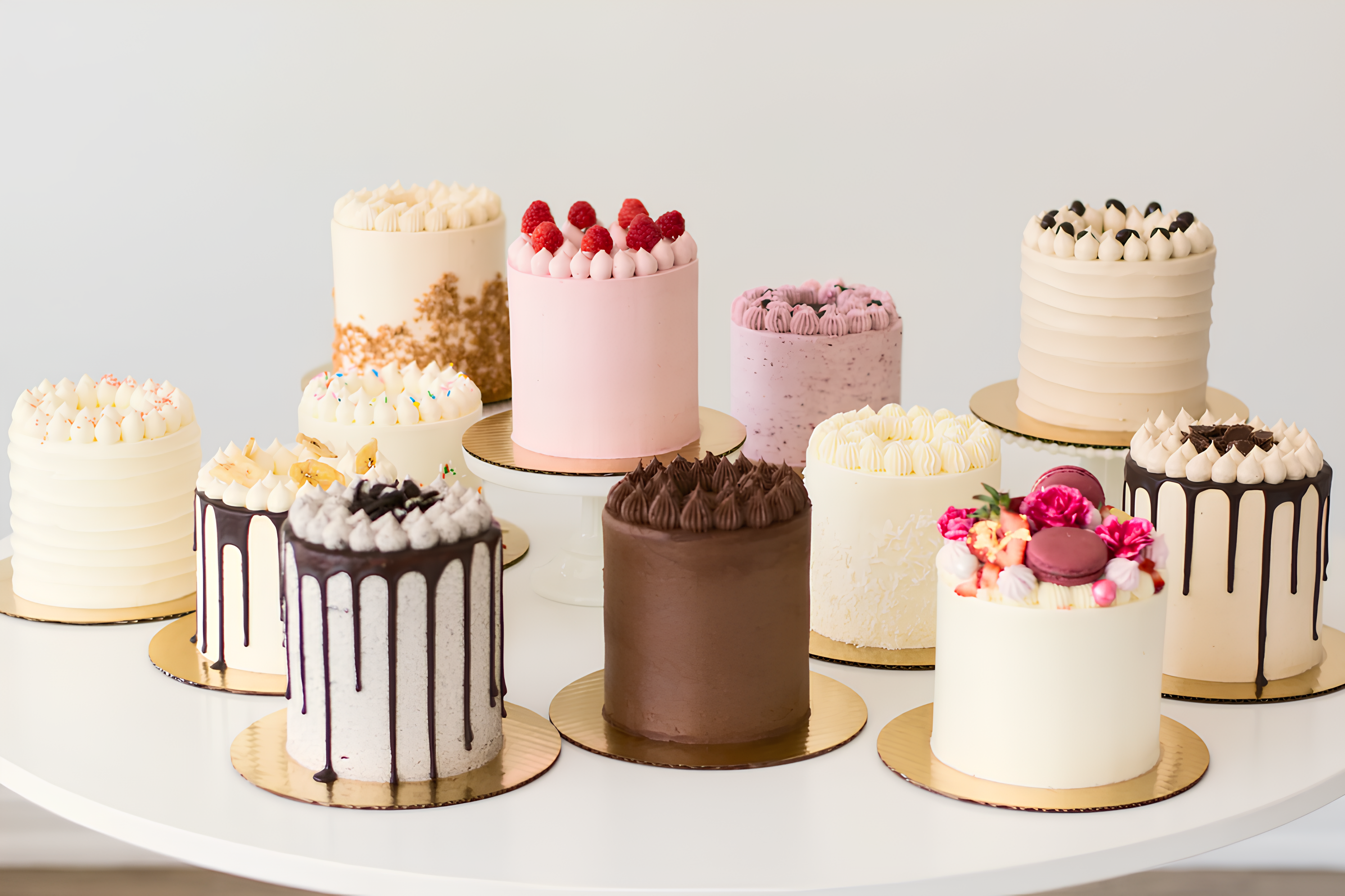 twelve tall cakes sitting on cake stands or cake boards on top of a white table